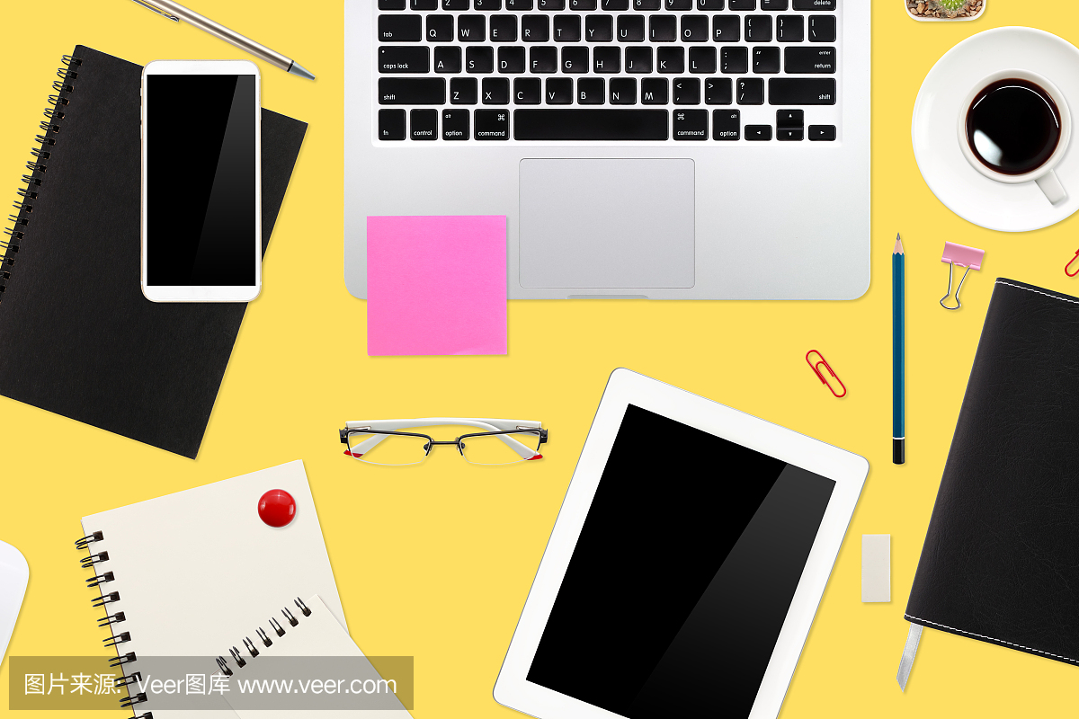 平铺的工作桌子上有笔记本电脑,办公用品,咖啡杯,平板电脑和手机在黄色柔和的背景